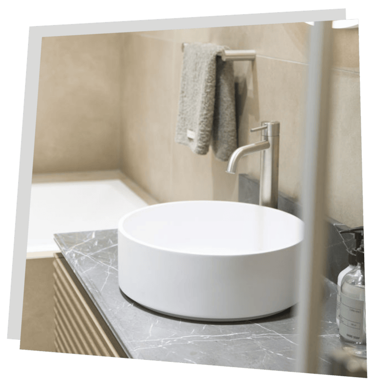 Beiges Bad mit weißem Keramikwaschbecken im vordergrund.