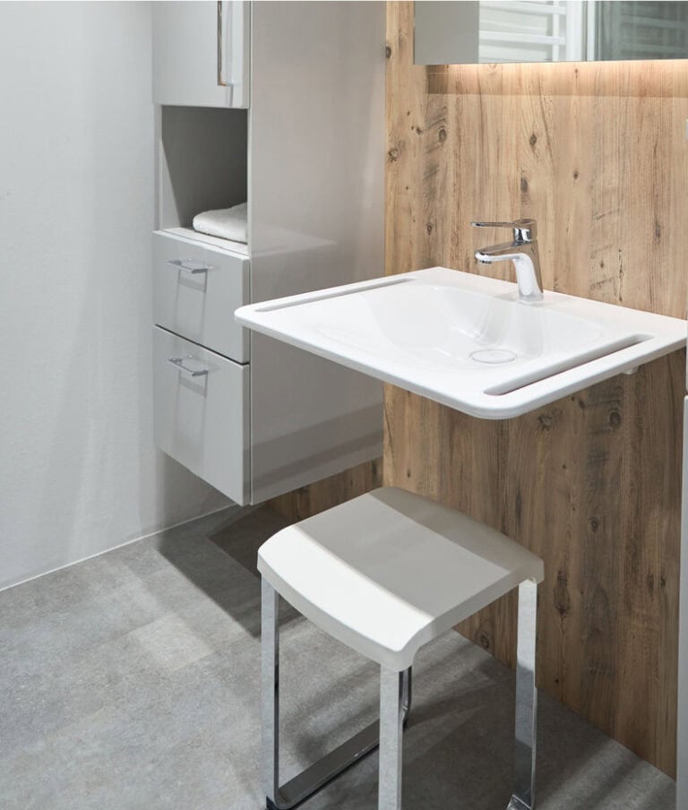 Barrierefreies Bad mit weißem Waschtisch und Stuhl.