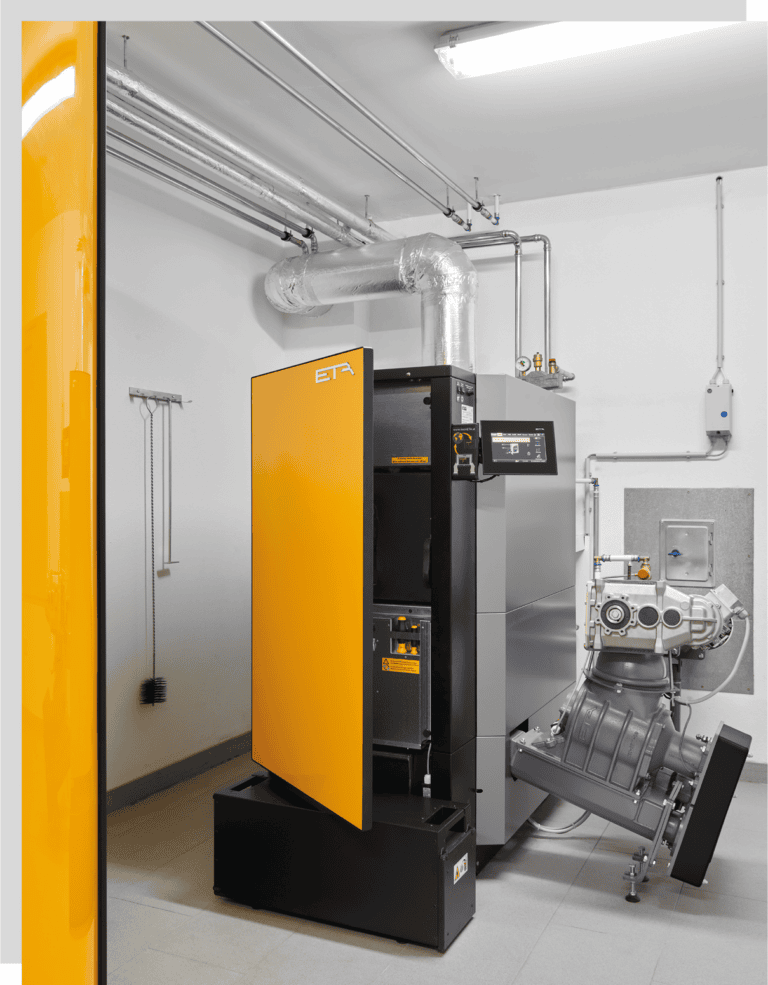 Palletheizung der Firma ETA mit orang-gelber Front. Sie steht im hellerleuchteten Kelleraum.