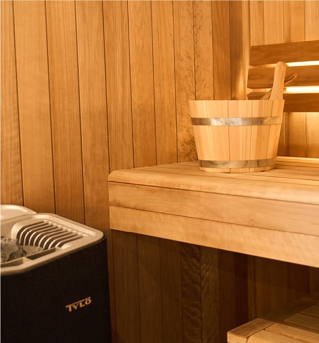 Wassereimer steht auf der Saunabank. Links davon ist der Saunaofen mit seinen Steinen platziert.