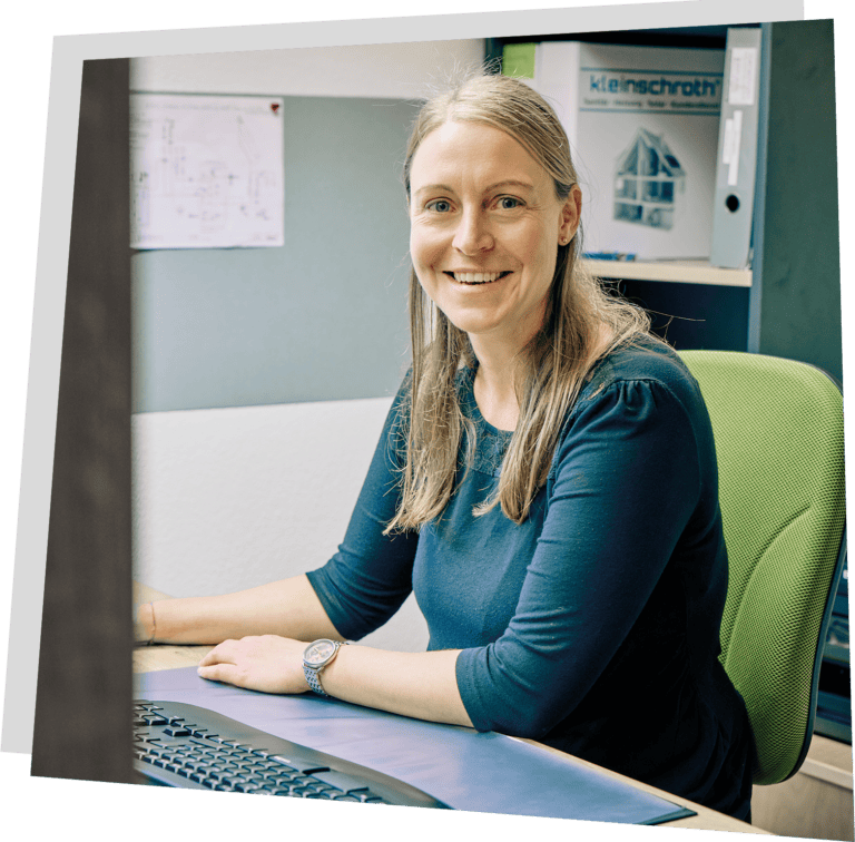 Mitarbeiterin von Kleinschroth Wärme mit blonden Haaren. Sie sitzt am Schreibtisch und lächelt in die Kamera.