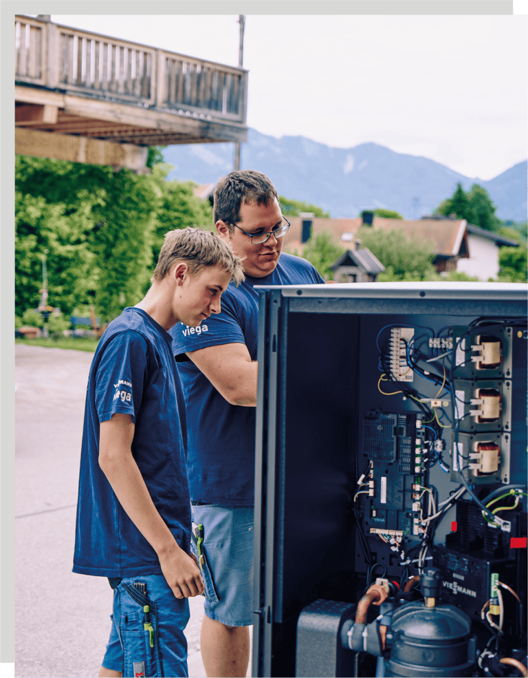 Zwei Mitarbeiter von Kleinschroth Wärme prüfen eine Wärmepumpe auf dem Firmengelände.