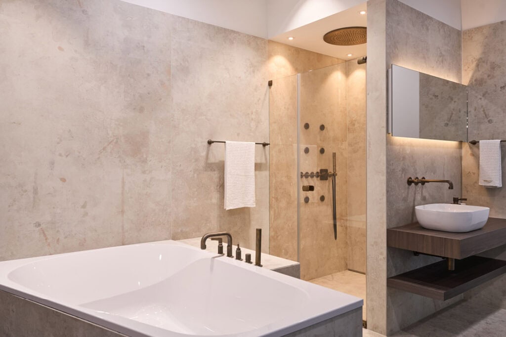 Freistehende, eckige Badewanne. Im Hintergrund befindet sich eine ebenerdige Dusche mit hochwertigen Armaturen aus Bronze.