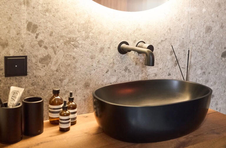 Aufgesetztes schwarzes Waschbecken mit Pflegeprodukte daneben.