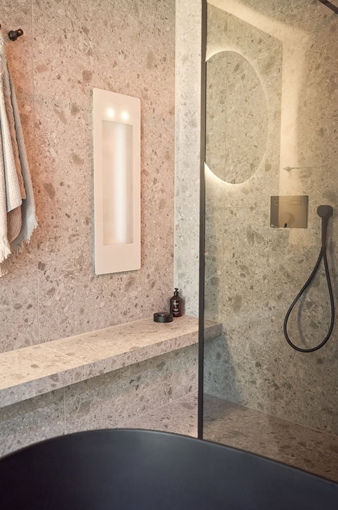 Ein Infrarotstrahler in einer Duschkabine. Im Vordergrund steht eine schwarze Badewanne.